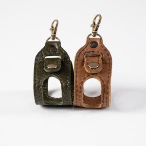 Handcrafted olive and brown leather Padel ball sling holder with brass lobster clasp and snap closure, holding a yellow Padel ball against a white background